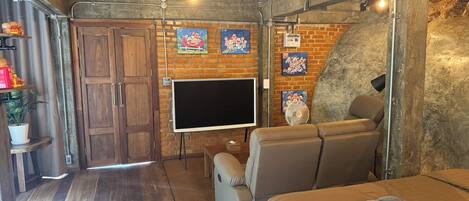 A cozy room with a brick wall, a flat-screen TV, a sofa, and a bed.