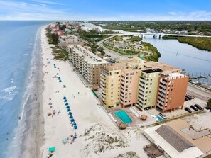 A beachfront hotel with multiple buildings, a swimming pool, and a beach with umbrellas.