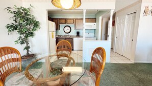 A dining area with a glass table surrounded by wicker chairs, a potted plant, and a hanging light fixture.