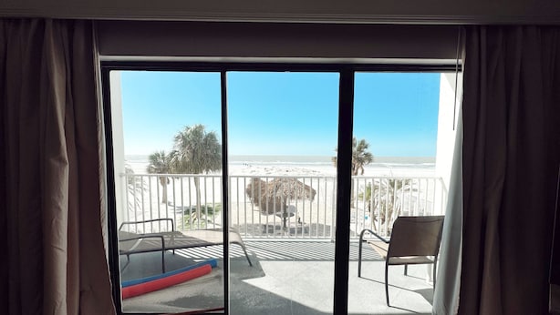 A room with a large sliding glass door leading to a balcony with a view of the beach.