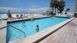 Una piscina con sillones de descanso, palmeras y cielo despejado.