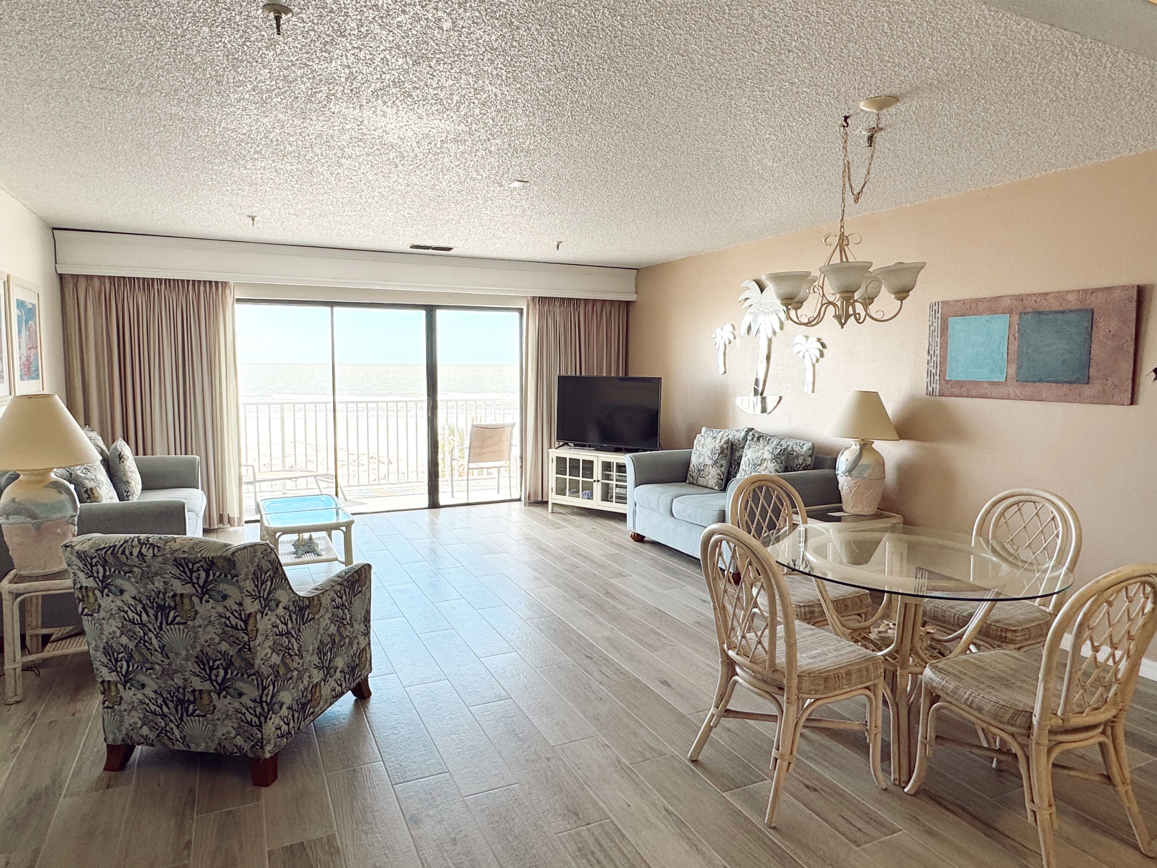 A spacious living room with a balcony, a television, and a dining area with wicker chairs.