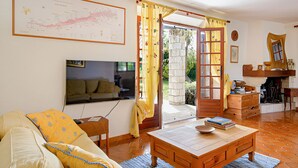 A living room with a sofa, coffee table, and a television. There is a doorway leading to an outdoor area with a stone pillar and a wooden door.