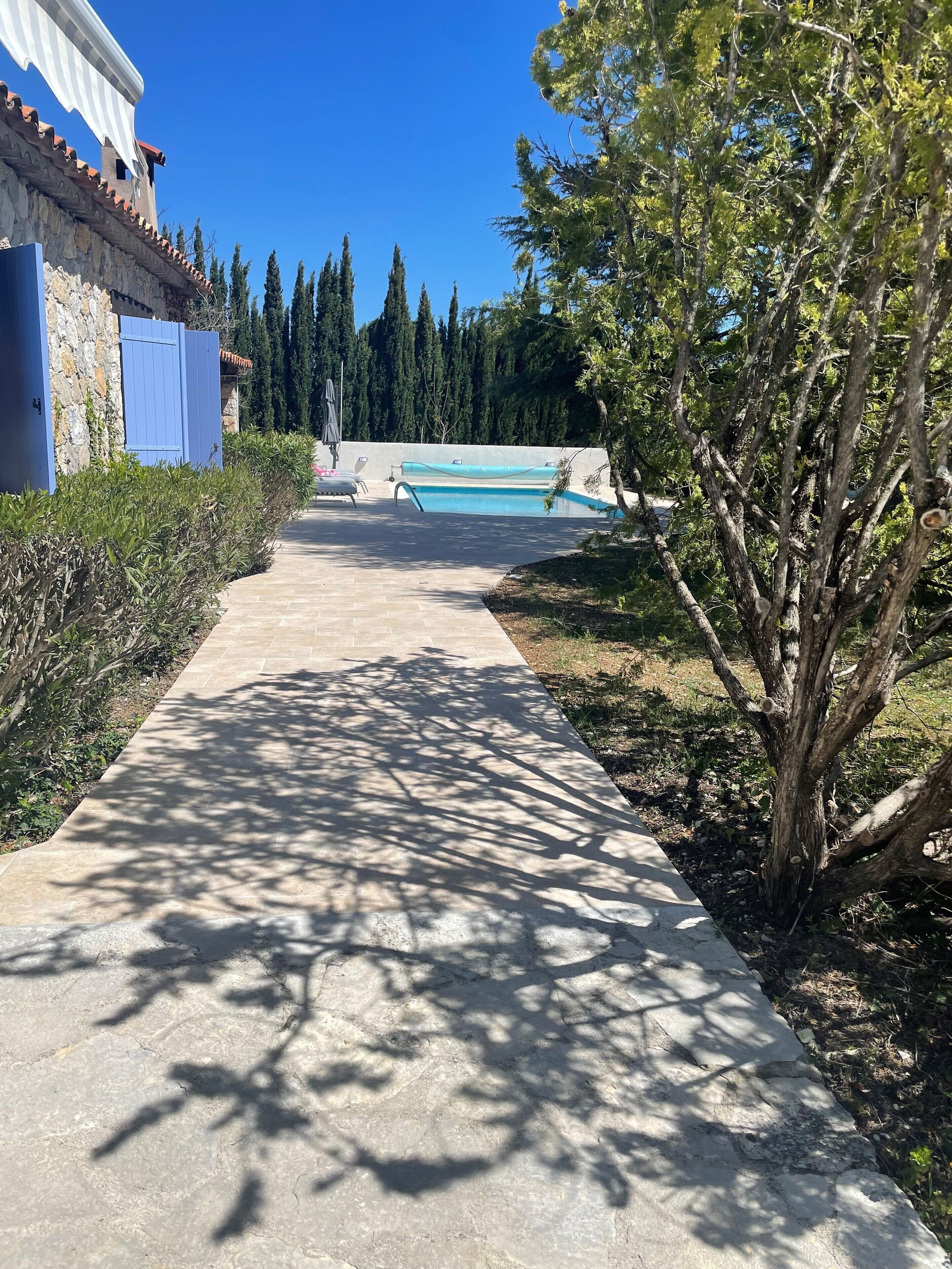 A pathway leading to a swimming pool with a stone wall and a blue building on the left.