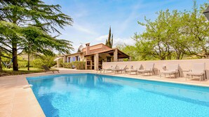 A swimming pool with lounge chairs, a covered patio, and a building with a tiled roof.