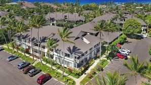 A multi-story hotel with a parking lot, surrounded by palm trees and a view of the ocean. - 2 Bedroom Condo in Poipu with Pool, Hot Tub, AC, Just steps to the Beach & Pools (Koloa)