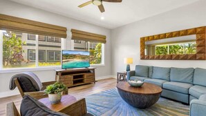 A modern living room with a television, sofa, coffee table, and a ceiling fan. - 2 Bedroom Condo in Poipu with Pool, Hot Tub, AC, Just steps to the Beach & Pools (Koloa)