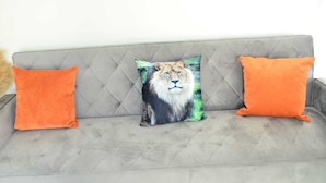 A grey tufted sofa with three orange cushions, one featuring a lion print. - Blok 3 by SB Stayz (Blackpool)