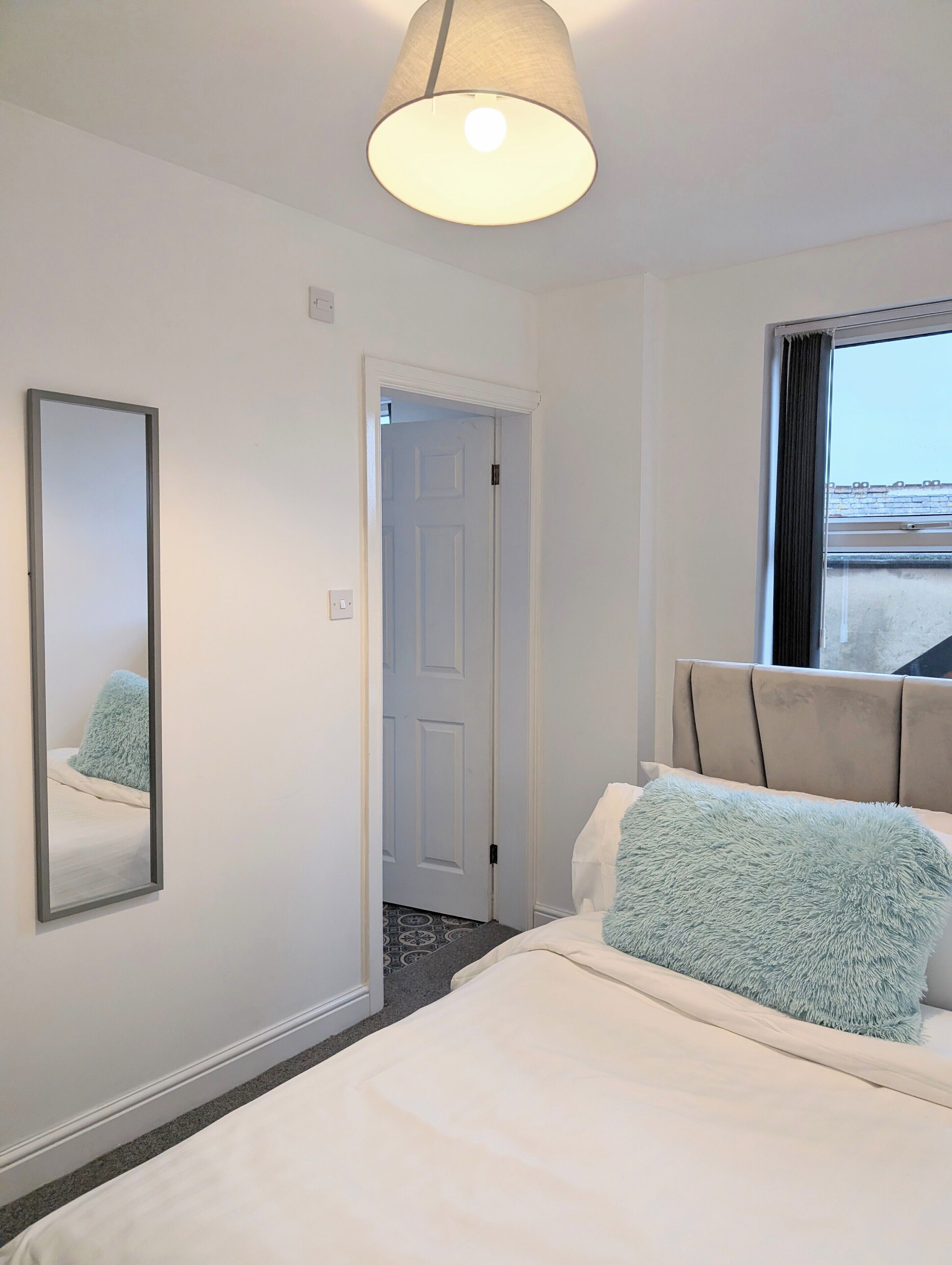 A hotel room with a bed, a large mirror, a door, and a window.
