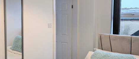 A hotel room with a bed, a large mirror, a door, and a window.
