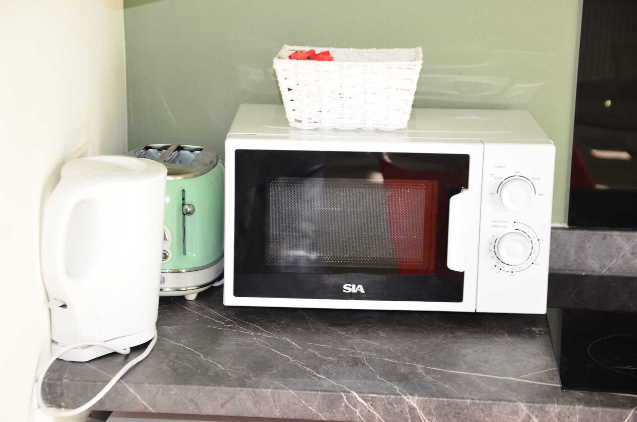 Un horno microondas blanco con una cesta encima, un tostador y un electrodoméstico blanco sobre una encimera de mármol.