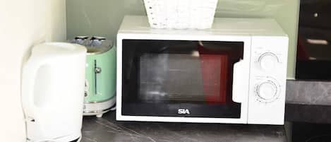 Un four à micro-ondes blanc avec un panier sur le dessus, un grille-pain et un appareil blanc posé sur un plan de travail en marbre.