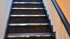 A staircase with black carpeted steps and a black handrail, leading to an open door at the top. - Blok 3 by SB Stayz (Blackpool)
