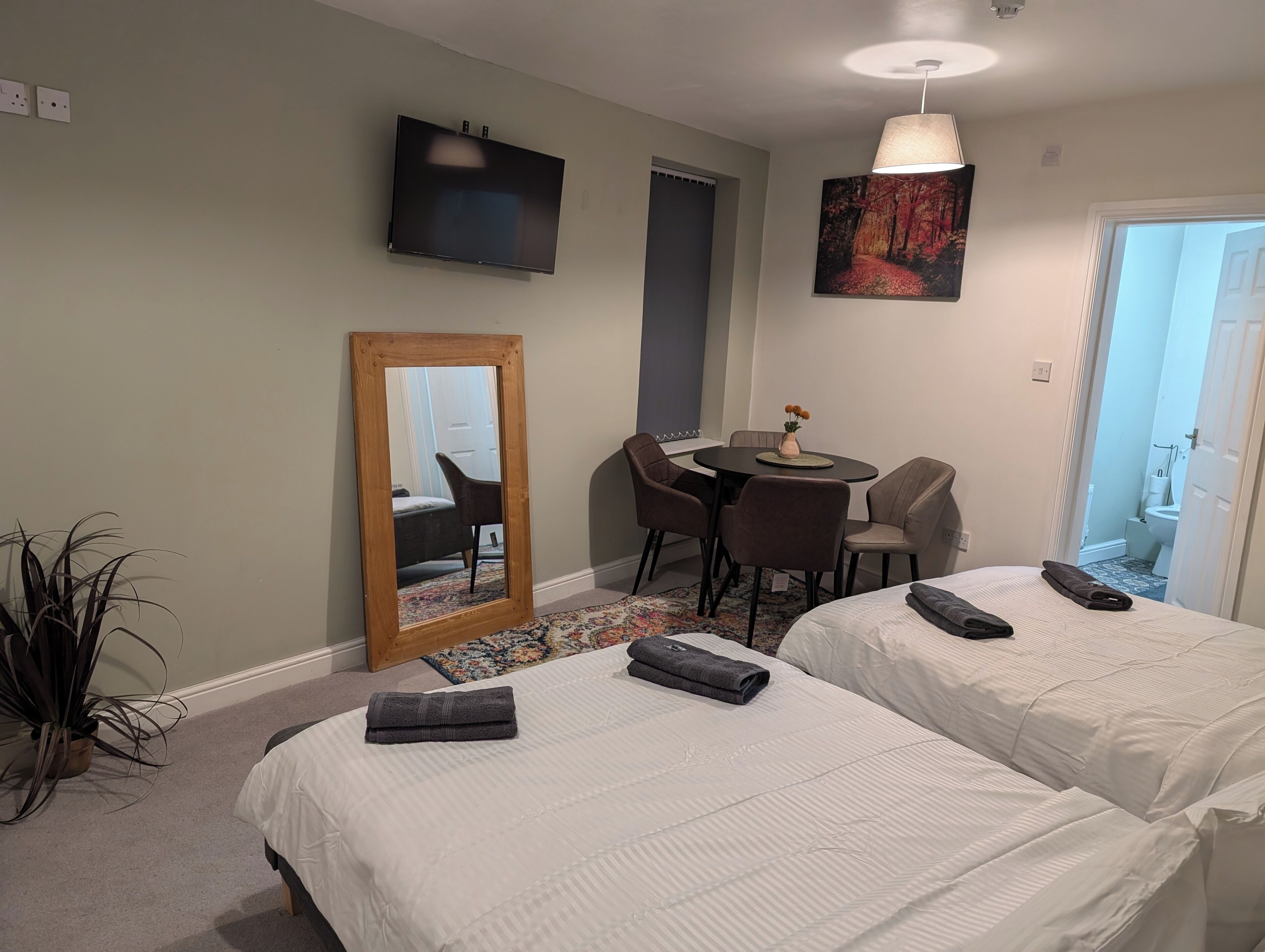 Habitación de hotel con dos camas, televisión, mesa de comedor con sillas, espejo y un cuadro en la pared.