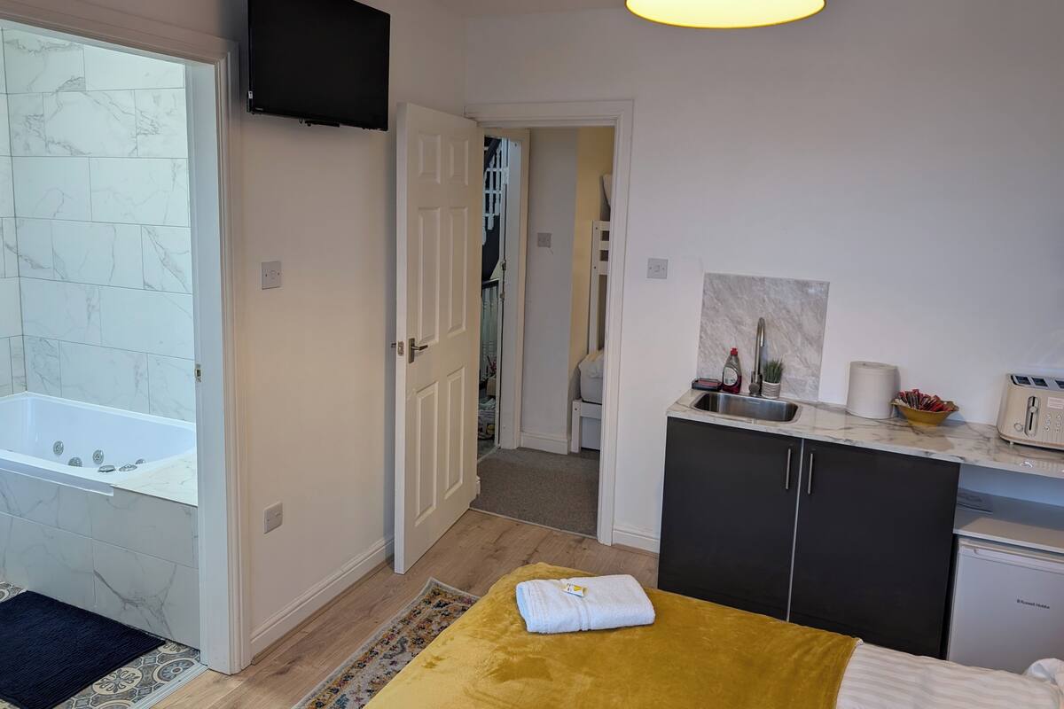 A modern bathroom with a bathtub, a shower, and a toilet. There is a sink with a mirror and a towel rack. The room has a yellow rug and a ceiling light.