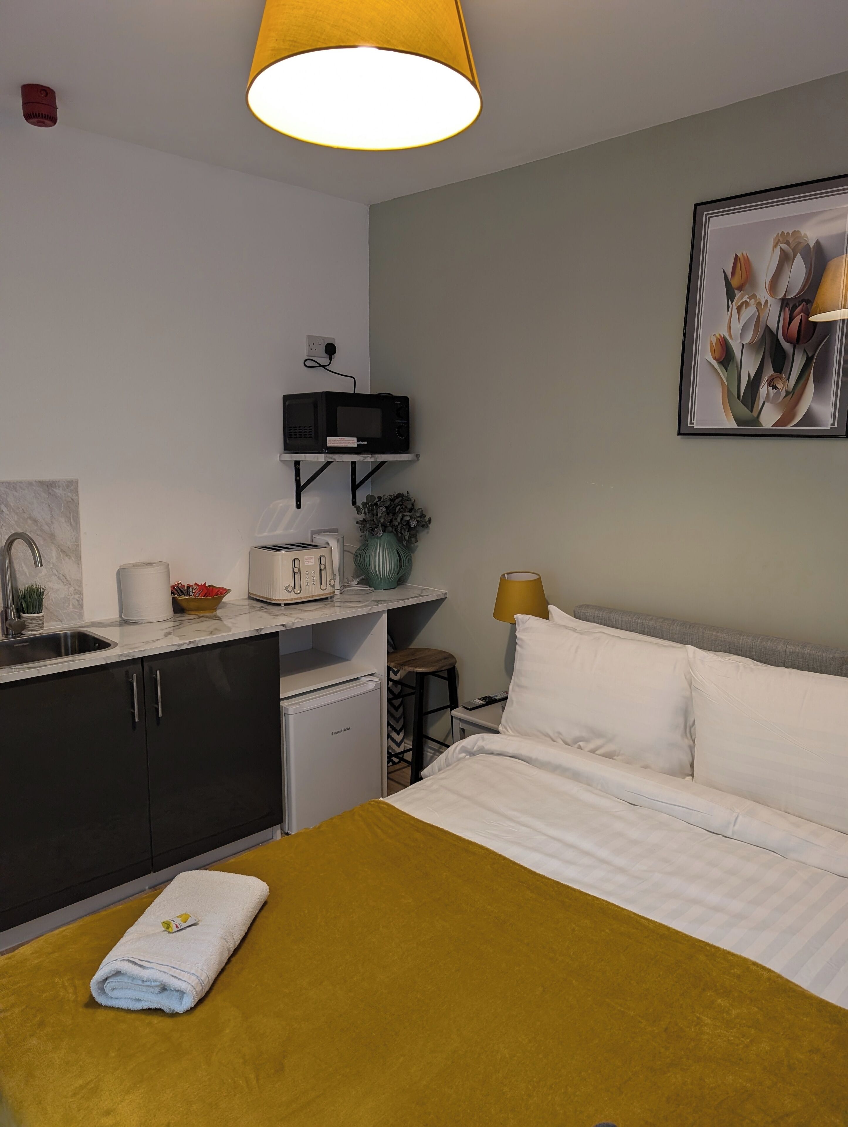 A compact hotel room with a bed, a small kitchenette, a sink, and a microwave.