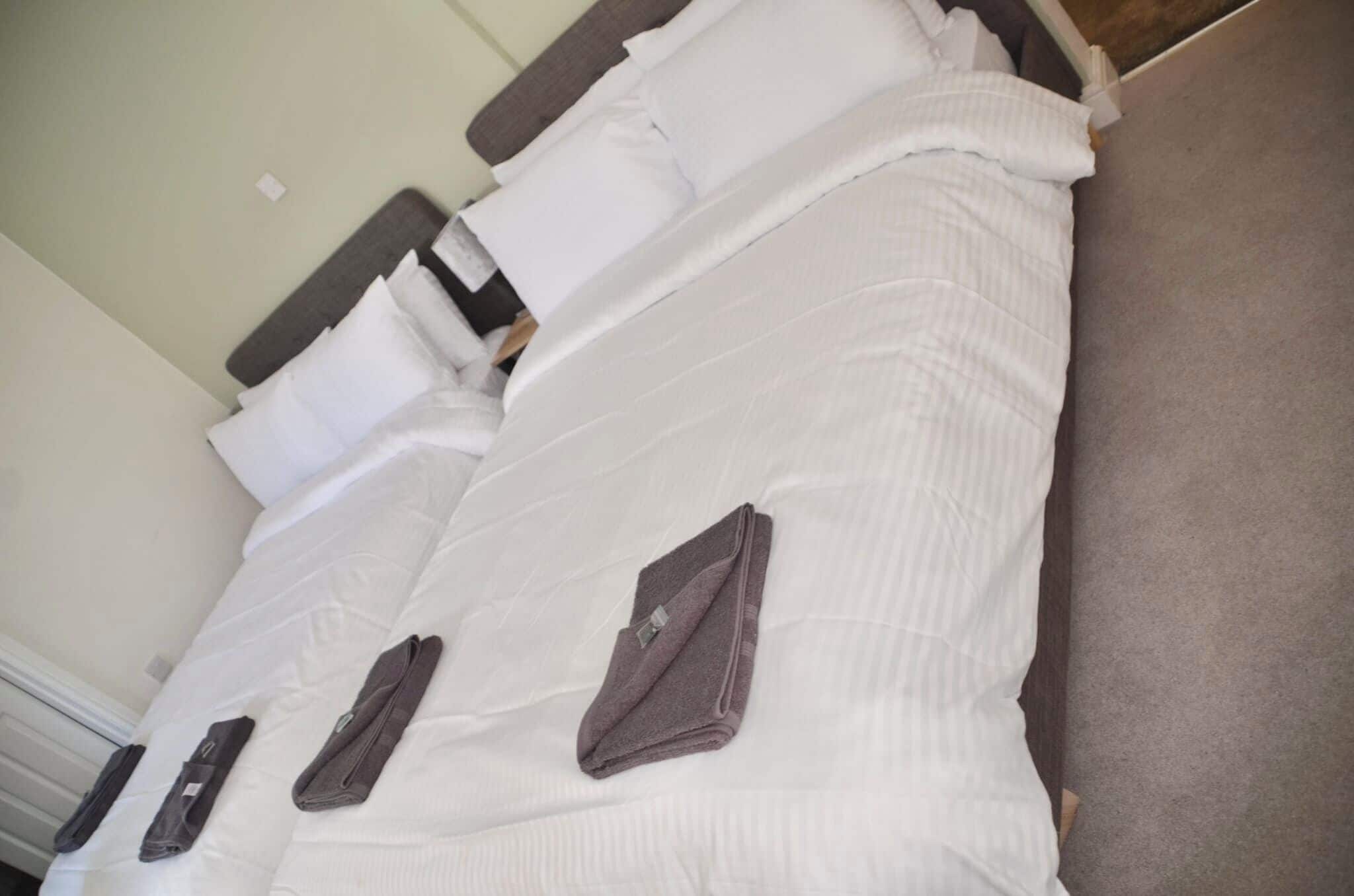 A hotel room with two beds, each with white linens and pillows. There are folded towels on the beds.
