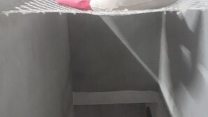 A narrow, enclosed space with a sloped ceiling, a white pillow on a shelf, and a small, dark object on the floor. - Cat boarding 🐱 Travel  (Maracanã Jarinu)