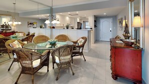 A modern kitchen with white cabinets, a central island, and a dining area with wicker chairs and a glass table.