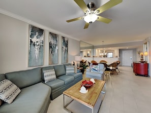Ein modernes Wohnzimmer mit einem grauen Sofa, einem Holztisch und einem Deckenventilator.