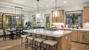 Una cocina moderna con una isla grande, taburetes de bar, armarios de madera e iluminación colgante.