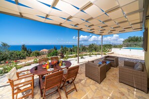 Un espace extérieur abrité, aménagé pour les repas, avec une table pour deux, des meubles en osier et une vue sur la mer.