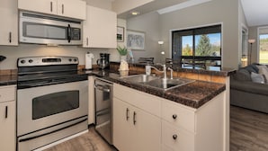 A modern kitchen with stainless steel appliances, a granite countertop, and a large window offering a view of the outdoors.