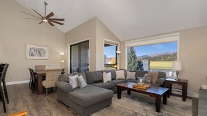 A spacious living room with a gray sectional sofa, a wooden coffee table, and a dining area with a table and chairs.