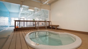 A hot tub in a spacious indoor area with wooden flooring and a high ceiling.