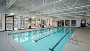 An indoor swimming pool with clear lanes, a metal ladder, and lounge chairs by the poolside.