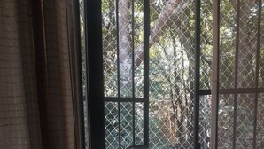 Una stanza con un'ampia finestra, tende e vista su uno spazio esterno con recinzione e alberi.
