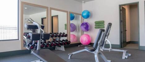 A gym with exercise equipment, a bench, dumbbells, and exercise balls.