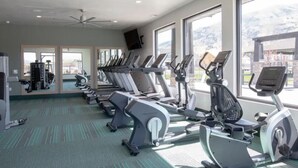 Un gimnasio con cintas de correr, bicicletas estáticas y un ventilador de techo.
