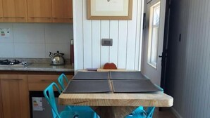 A kitchen with wooden cabinets, a dining table with blue chairs, a framed picture on the wall, and a window. - Casa Pumahue  (Puerto Varas)