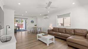 Ein modernes Wohnzimmer mit einem braunen Ledersofa, weißen Möbeln, einem Essbereich mit Tisch und Stühlen sowie einem Deckenventilator.