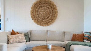 A living room with a light-colored sofa, a round wooden coffee table, and a woven wall hanging. - The Beach House 64 Neighbour Ave Goolwa Beach (Goolwa)