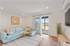 Un salon avec un canapé bleu clair, une petite table ronde, une grande fenêtre donnant sur un beau paysage et une œuvre d’art accrochée au mur.