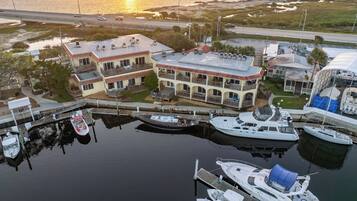 A marina with boats docked, a large building with balconies, and a sunset in the background.