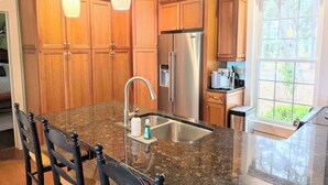 A kitchen with wooden cabinets, a stainless steel refrigerator, granite countertops, and pendant lighting. - JonBie Maisons SEA GLASS COTTAGE cart included with booking (Daufuskie Island)