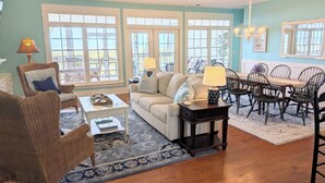 A spacious living room with a large window, a ceiling fan, and a dining area with a table and chairs. - JonBie Maisons SEA GLASS COTTAGE cart included with booking (Daufuskie Island)
