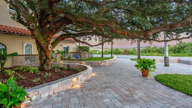 A paved walkway with a tree-lined path, a stone planter, and a building with a red-tiled roof. - Garden View Studio | King Bed + Patio | Pet-Friendly (St. Augustine)