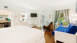 Een slaapkamer met een bed, een dressoir, een televisie, een raam met gordijnen en uitzicht op het landschap.