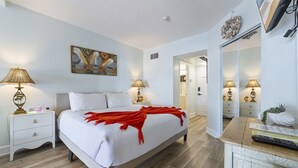 A well-lit bedroom with a bed, bedside tables, lamps, a painting, and a mirror.