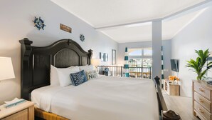 A hotel room with a large bed, a nightstand, a desk with a chair, a potted plant, and a view of the marina through the window. - Pet Friendly King Studio with Harbor Views (St. Augustine)