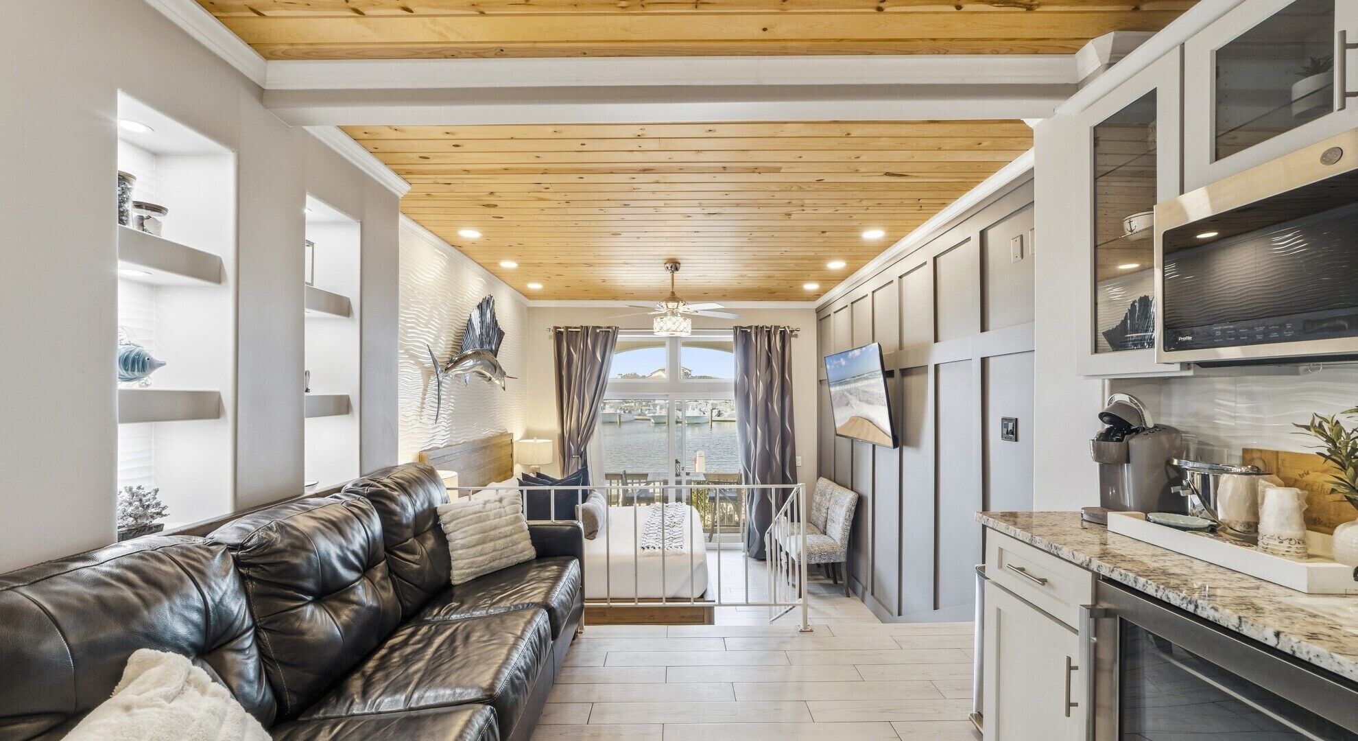 A modern kitchen with a marble countertop, a black leather sofa, and a view of the marina through large windows.