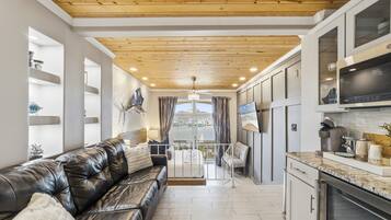 A modern kitchen with a marble countertop, a black leather sofa, and a view of the marina through large windows.