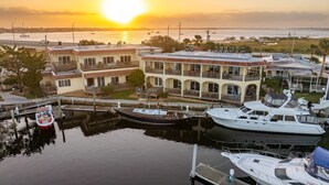 A marina with several boats docked, a building with multiple balconies overlooking the water, and a sunset in the background. - Harbor View Studio | King Bed + Covered Balcony | Dogs OK (St. Augustine)