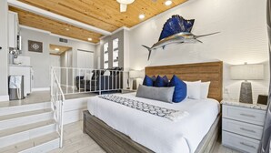 A modern bedroom with a large bed, a wooden headboard, and a decorative fish sculpture on the wall. - Harbor View Studio | King Bed + Covered Balcony | Dogs OK (St. Augustine)