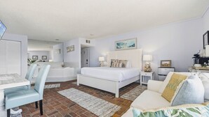 A hotel room with a bed, a desk, a chair, a small table, a lamp, and a painting on the wall.