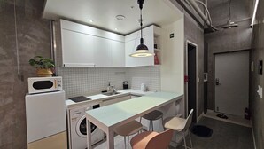 Une cuisine compacte équipée d’un lave-linge intégré, d’un four à micro-ondes et d’un évier. On y trouve deux tabourets de bar et un luminaire suspendu.